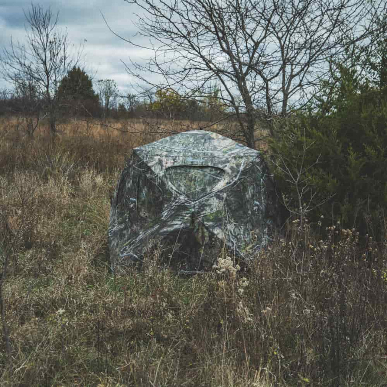 Ameristep Silent Brickhouse 59x59 pop-up ground blind in Mossy Oak camouflage set up in open field with trees and brush in the background