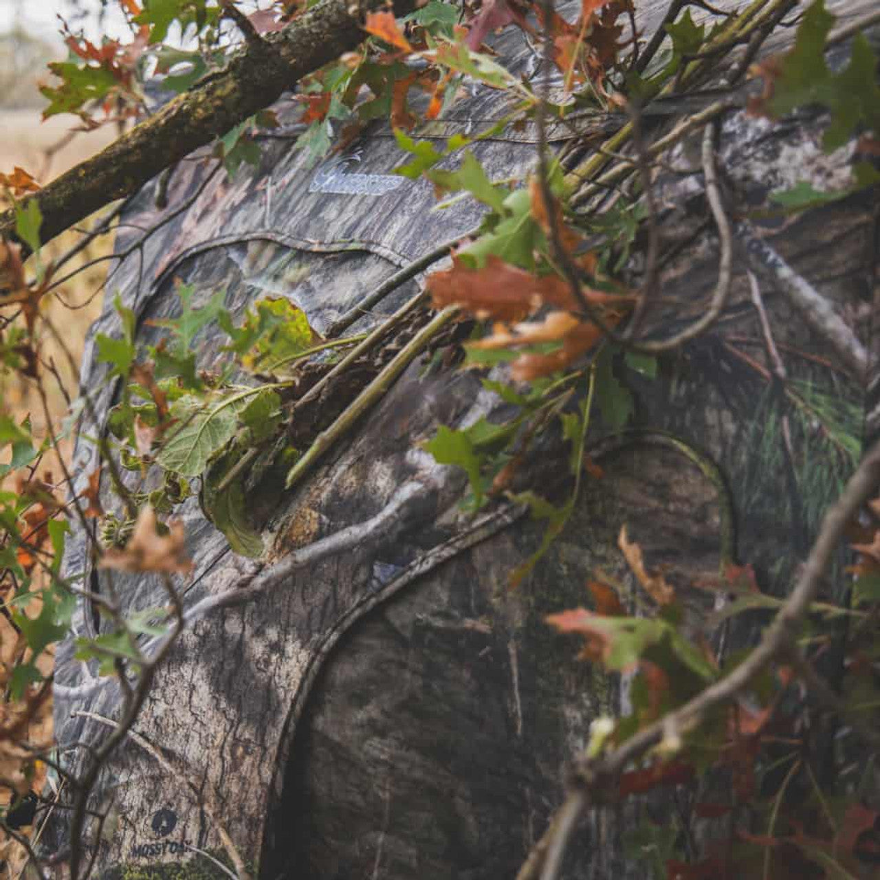 Ameristep Silent Brickhouse 59x59 pop-up ground blind in Mossy Oak camouflage partially concealed with branches and leaves in a wooded setting