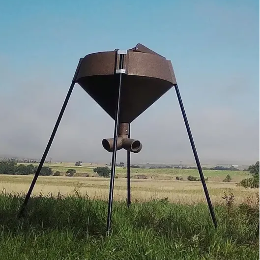 Boss Buck 600 lb Gravity Deer Feeder in open pasture — tan rotomolded gravity feeder with 3-way feed head and tripod steel legs for reliable deer feeding.