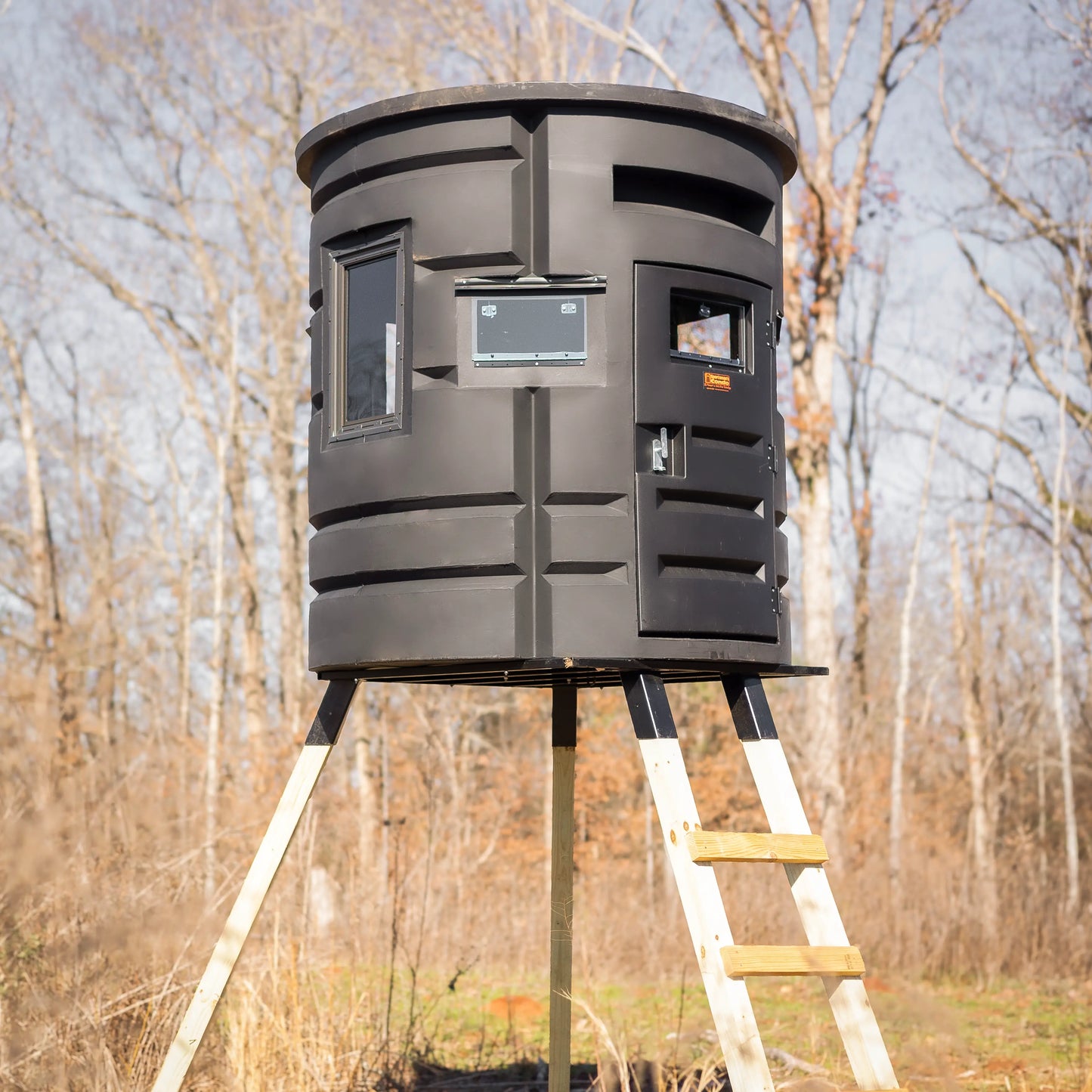 Angled close-up of Sportsman Bow Condo elevated deer blind with entry door and ladder in wooded area