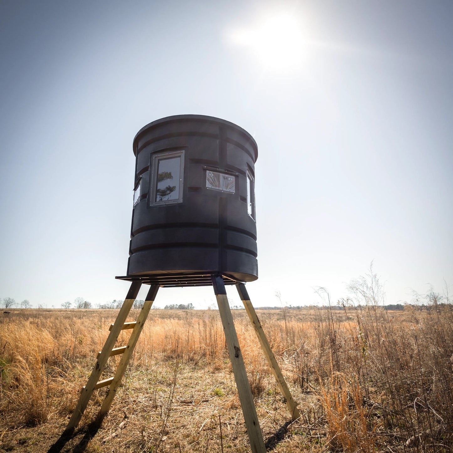 Front view of Sportsman Bow Condo elevated deer blind with ladder in an open field under bright sun