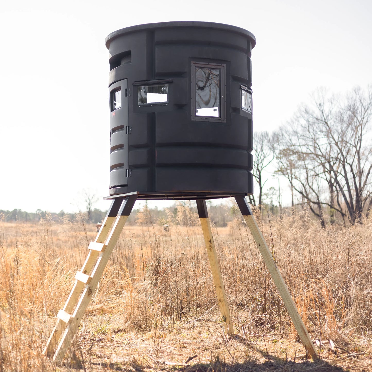 Side view of Sportsman Bow Condo deer blind elevated on wooden legs in an open field