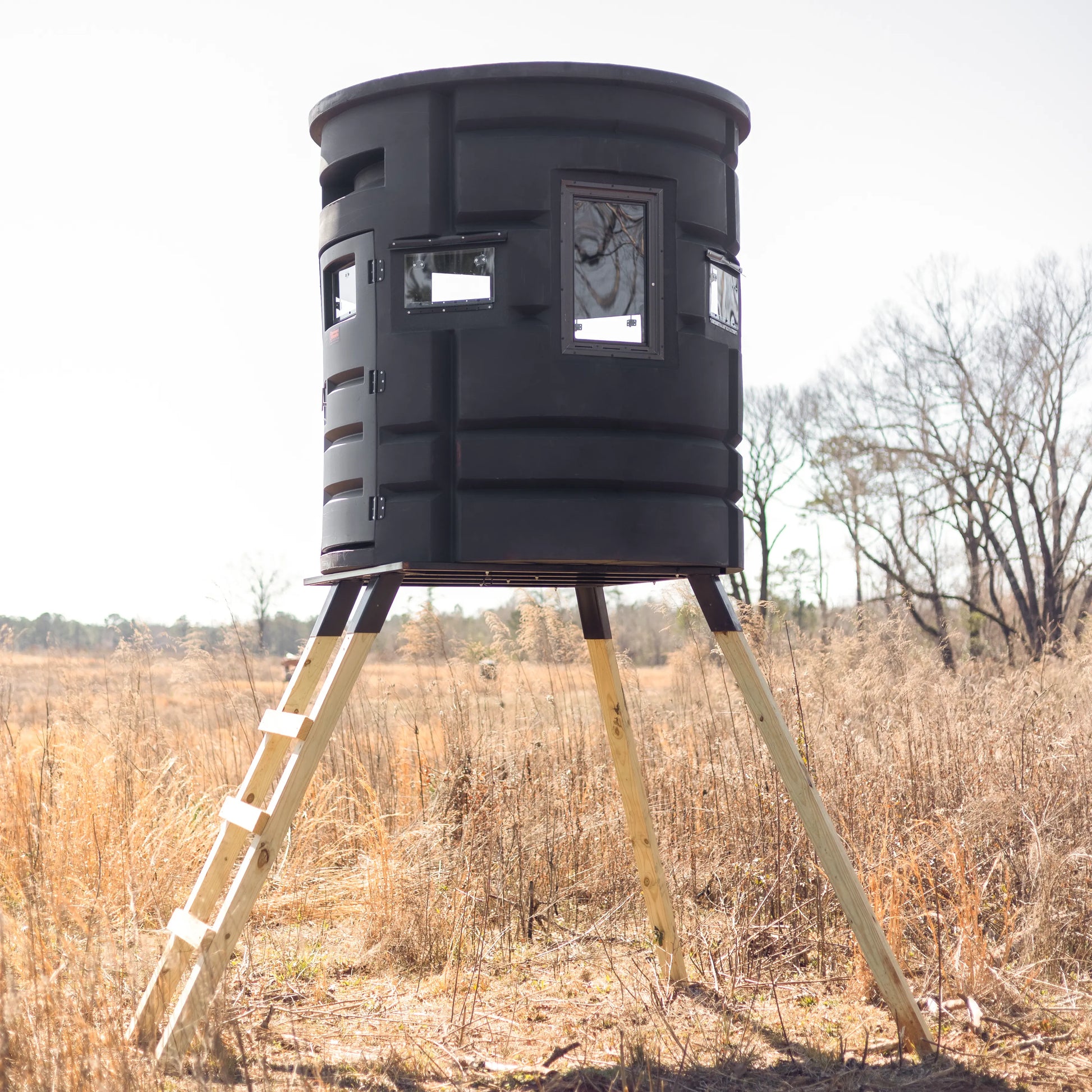 Side view of Sportsman Bow Condo deer blind elevated on wooden legs in an open field