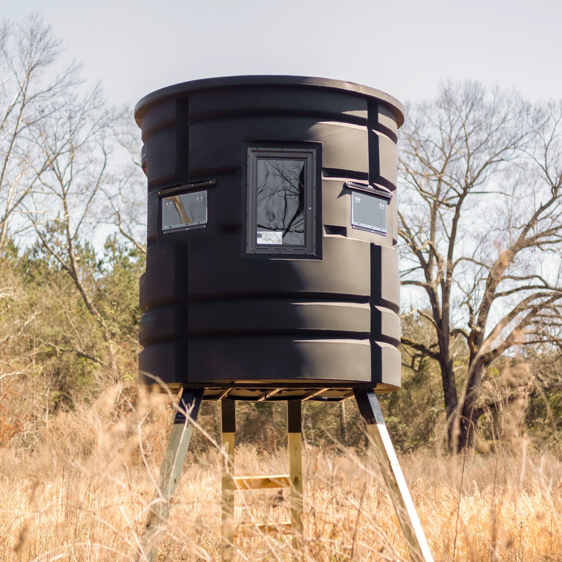 Full-height view of Sportsman Bow Condo deer blind elevated on wooden platform in open field