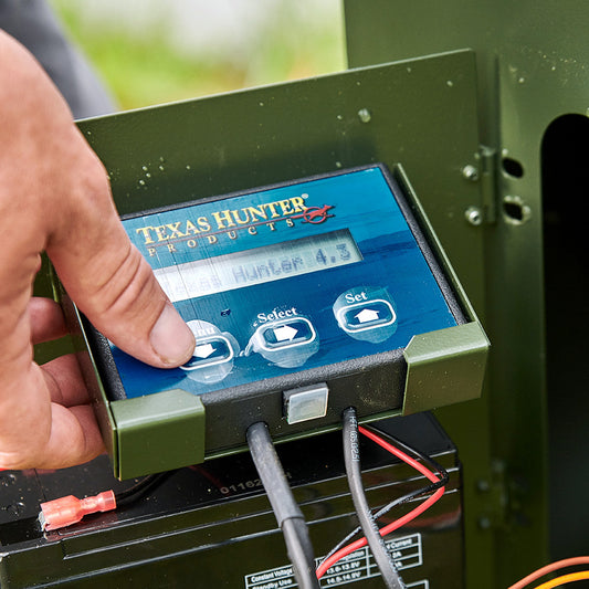 Close-up of a person adjusting a Texas Hunter digital timer on a fish feeder.