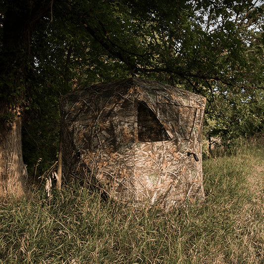 Camouflage hunting blind in a grassy field with trees