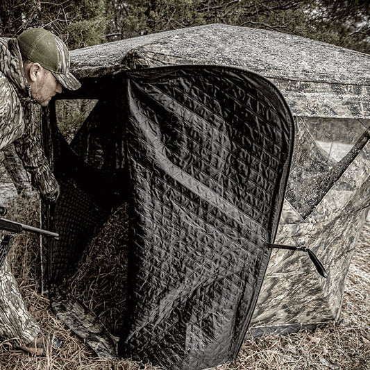 Ameristep Pro Series Insulated 59x59 pop-up ground blind with hunter in camouflage gear entering through zippered door in a wooded field