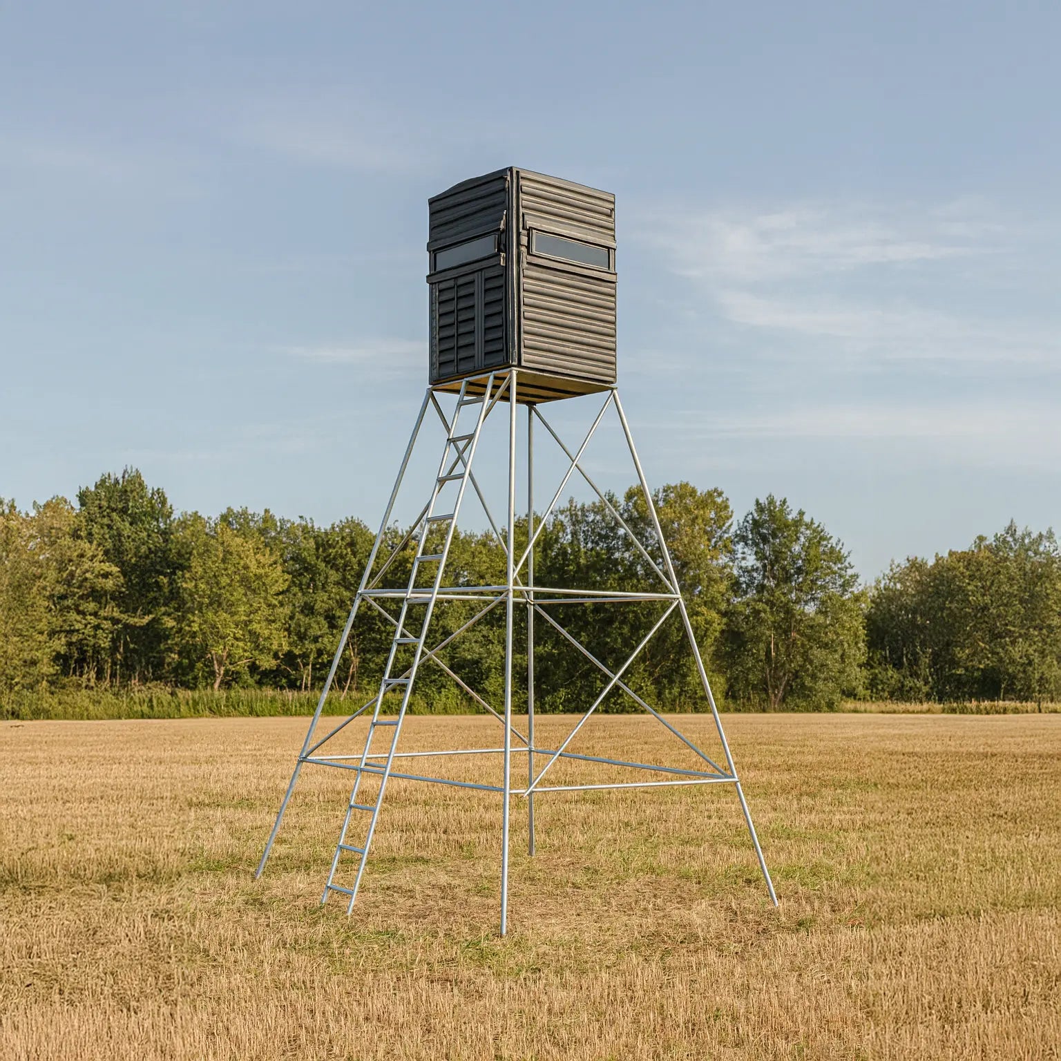 Side profile of The Blynd 4x4 Bow Hunting Deer Blind on tall steel stand in a grassy field, ideal for maximizing hunting visibility.

