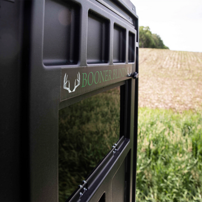 Close-up of Booner 5-Panel deer hunting blind window and exterior paneling with Booner Blinds logo in a field setting, sold by Outdoors For Less