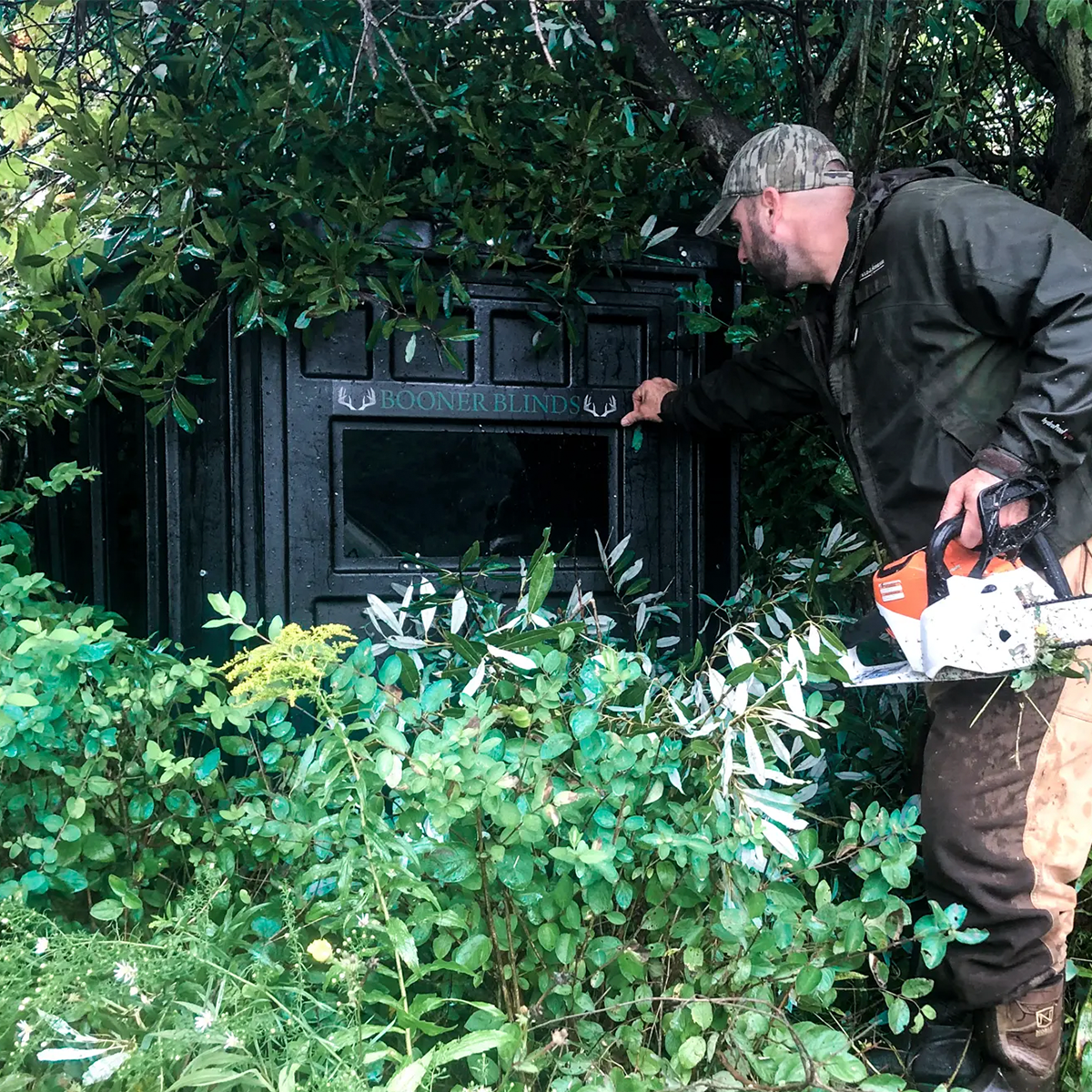 Hunter installing and brushing in a Booner 6-Panel deer hunting blind in heavy cover, concealed ground blind setup sold by Outdoors For Less