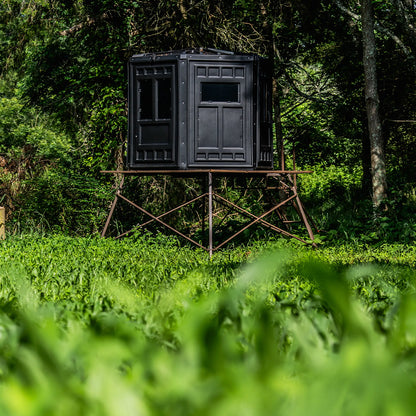 Booner 6-Panel deer hunting blind elevated on a tower overlooking a green food plot, premium elevated blind setup sold by Outdoors For Less