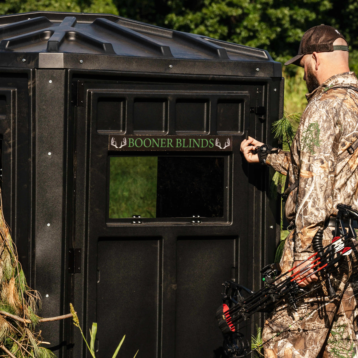 Bowhunter adjusting a shooting window on a Booner 6-Panel deer hunting blind with Booner Blinds logo visible, ground blind setup sold by Outdoors For Less