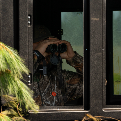 Hunter glassing with binoculars inside a Booner 6-Panel deer hunting blind, interior view through shooting windows sold by Outdoors For Less