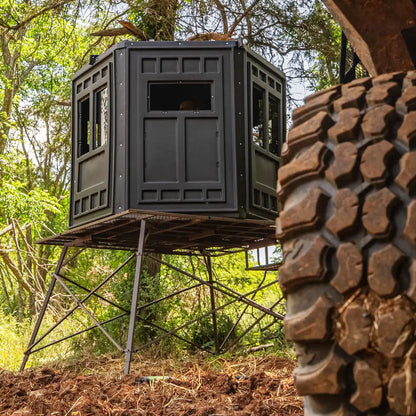 Booner 6-Panel deer hunting blind elevated on a steel tower in a wooded area, elevated hunting blind setup sold by Outdoors For Less