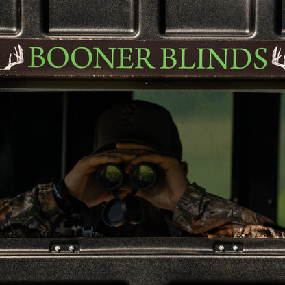Hunter using binoculars inside a Booner deer hunting blind with Booner Blinds logo visible, premium whitetail hunting blind sold by Outdoors For Less