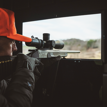 Rifle hunter aiming through a shooting window inside a Booner deer hunting blind, interior view highlighting stability and visibility sold by Outdoors For Less