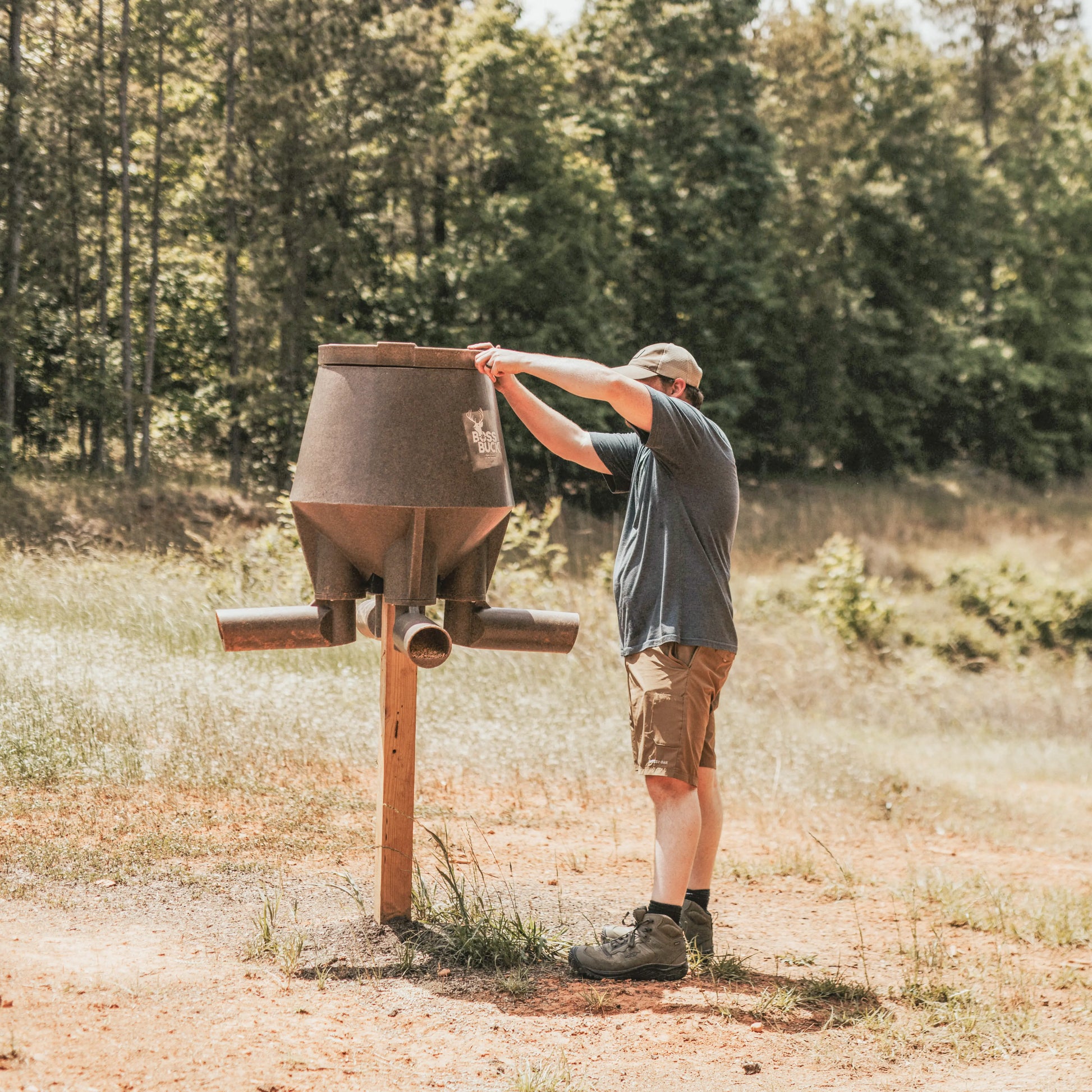 Hunter installing Boss Buck 200lb Post-Mounted Deer Feeder in open field — rugged rotomolded feeder designed for easy 4x4 post mounting and long-lasting outdoor use.