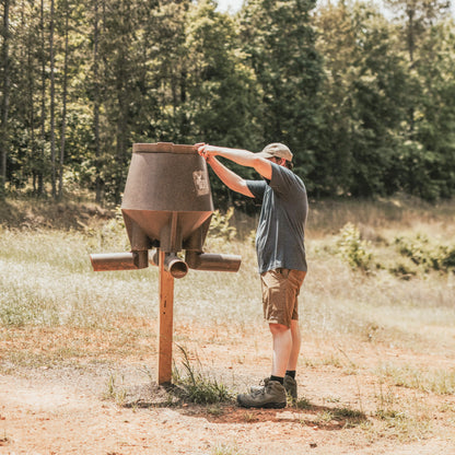 Hunter installing Boss Buck 200lb Post-Mounted Deer Feeder in open field — rugged rotomolded feeder designed for easy 4x4 post mounting and long-lasting outdoor use.