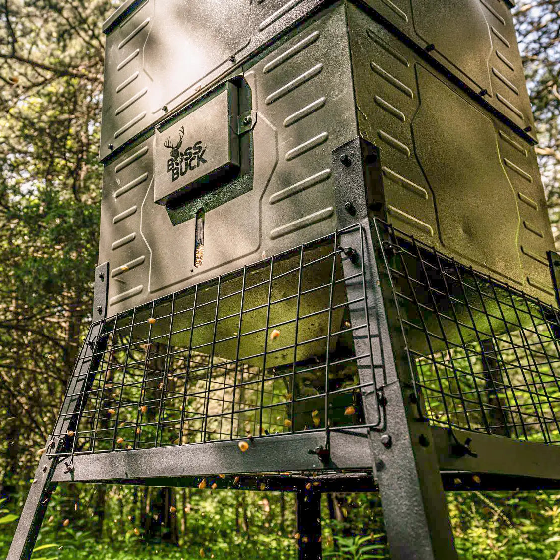 Boss Buck 300lb Stand & Fill Automatic Sled Deer Feeder in wooded area — tan rotomolded feeder with steel sled base, spinner plate, and digital timer for reliable deer feeding.