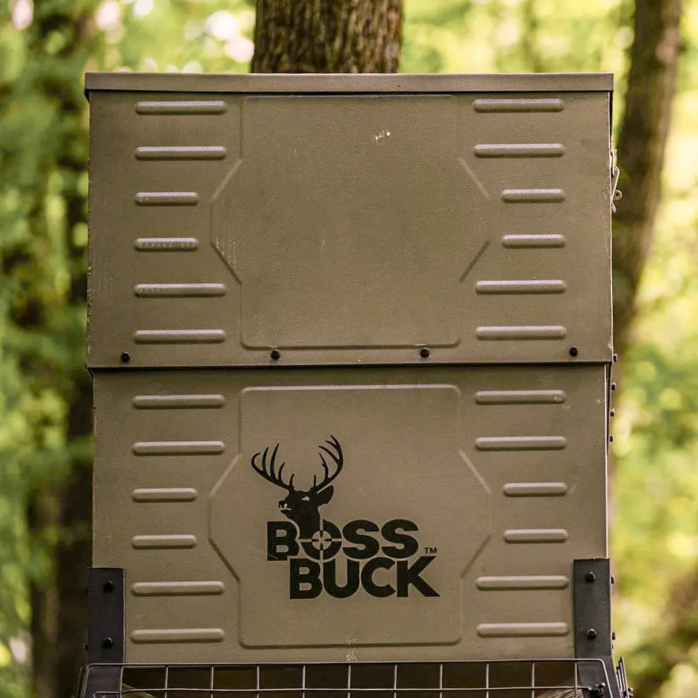 Boss Buck 300lb Stand & Fill Automatic Sled Deer Feeder placed in grassy hunting area — tan gravity feeder with steel sled base, digital timer, and weatherproof design for wildlife feeding.