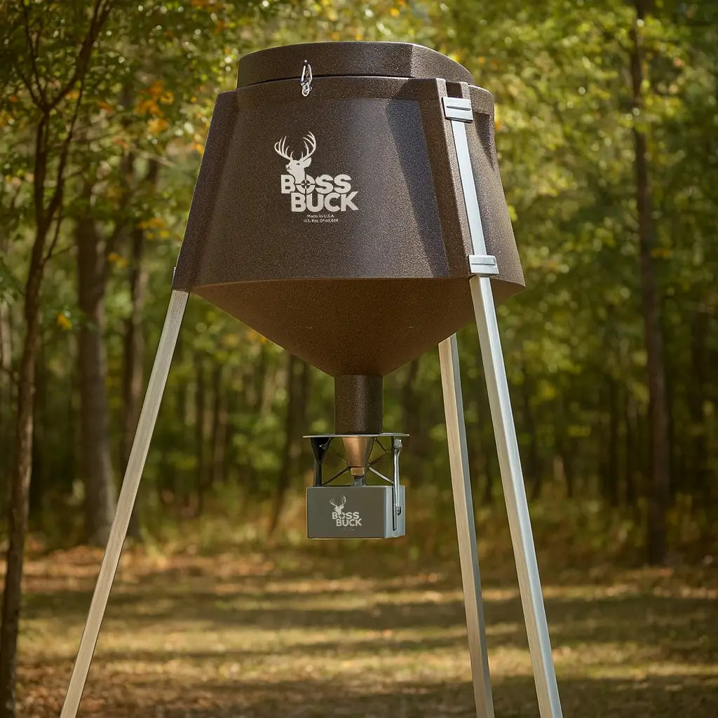 Boss Buck 350 lb Automatic Deer Feeder standing in wooded area — tripod-mounted brown feeder with automatic timer and spinner plate for deer feeding.