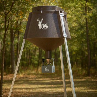 Boss Buck 350 lb Automatic Deer Feeder standing in wooded area — tripod-mounted brown feeder with automatic timer and spinner plate for deer feeding.