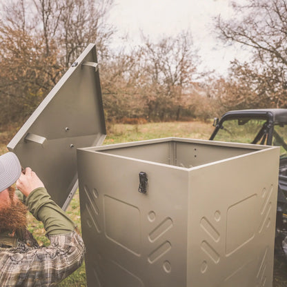 Boss Buck 600lb Stand & Fill Automatic Sled Deer Feeder being filled outdoors — large tan gravity hopper on skid base for easy transport and refill during hunting season.