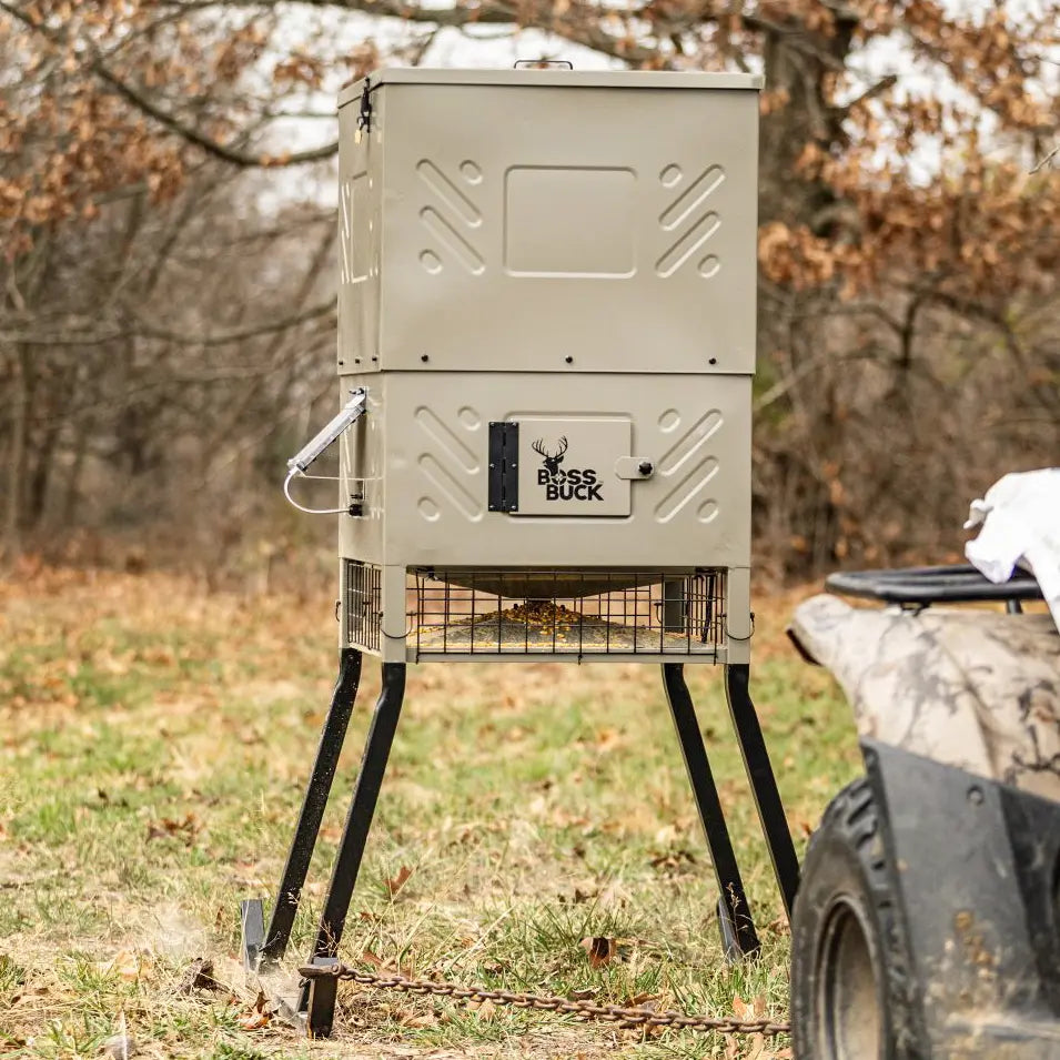 Boss Buck 600lb Stand & Fill Automatic Sled Deer Feeder set up in grassy field — tan rotomolded hopper on steel sled frame with 12-volt spinner system for reliable deer feeding.