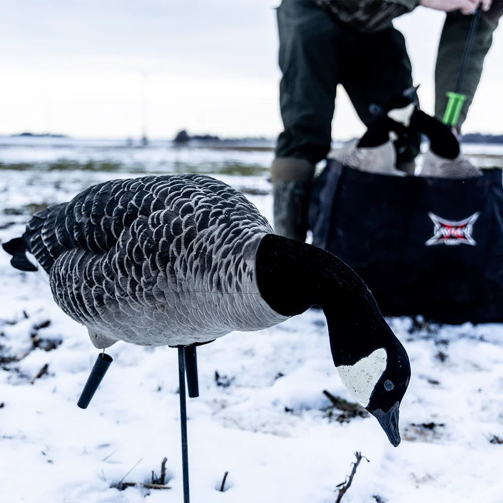 Avian-X AXF Lessers Outfitter Pack feeder goose decoy staked in snowy field with hunter and slot bag behind