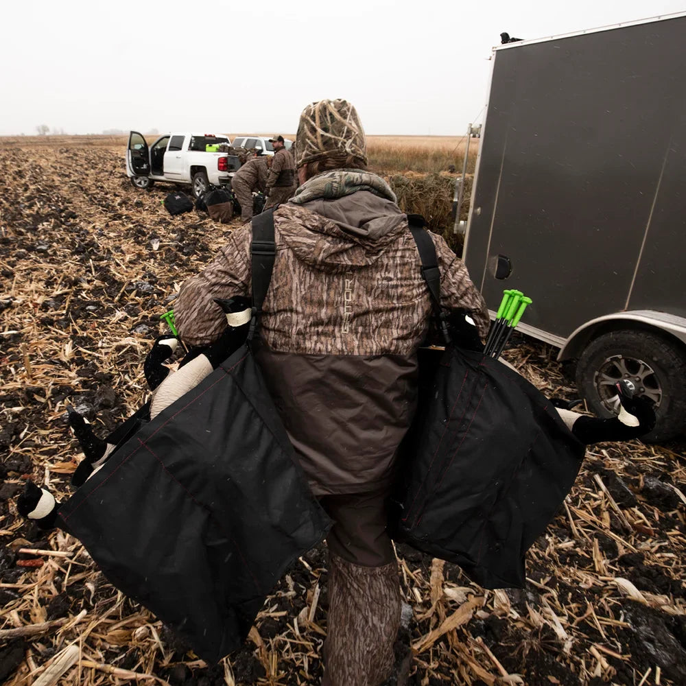 Hunter carrying Avian-X AXP Lessers Active Pack decoy bags to trailer in harvested field