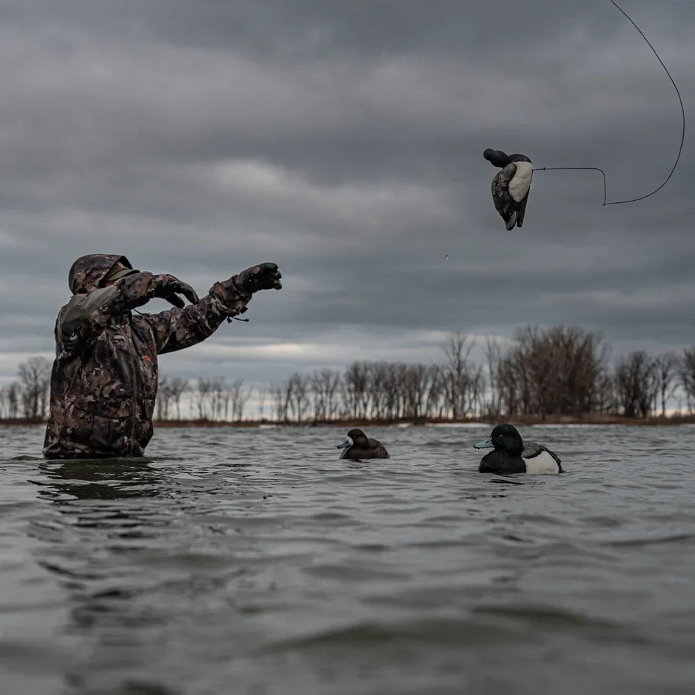 Camo-clad hunter tossing Avian-X TopFlight Bluebills decoy into spread on open water