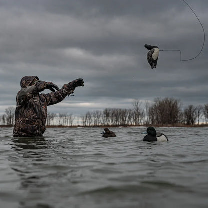Camo-clad hunter tossing Avian-X TopFlight Bluebills decoy into spread on open water