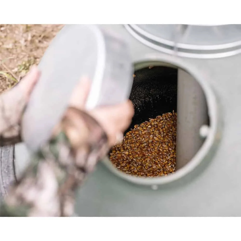 Capsule Feeders 100-LB Easy-Fill Game Feeder fill port open with person in camo loading corn grain into feeder