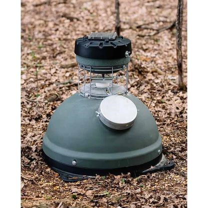Capsule Feeders 200-LB Easy-Fill Game Feeder with Base, placed on leaf-covered forest floor front view