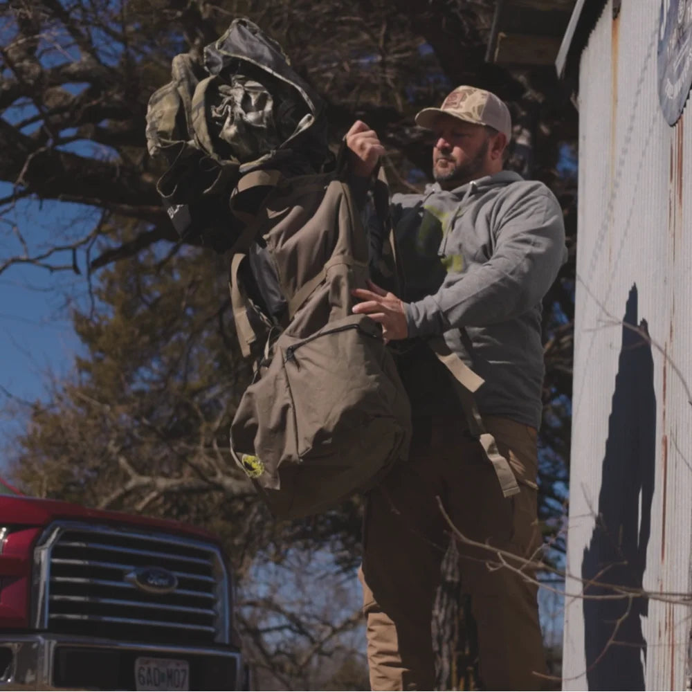 Horn Hunter Blind Hog Pack lifestyle shot, man holding and examining the pack outdoors near a building and truck