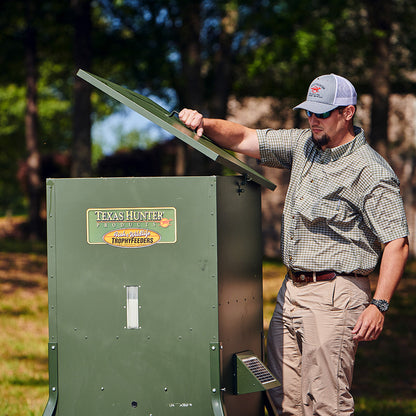 Man opening the lid of a Texas Hunter 425 lb feeder in an outdoor setting
