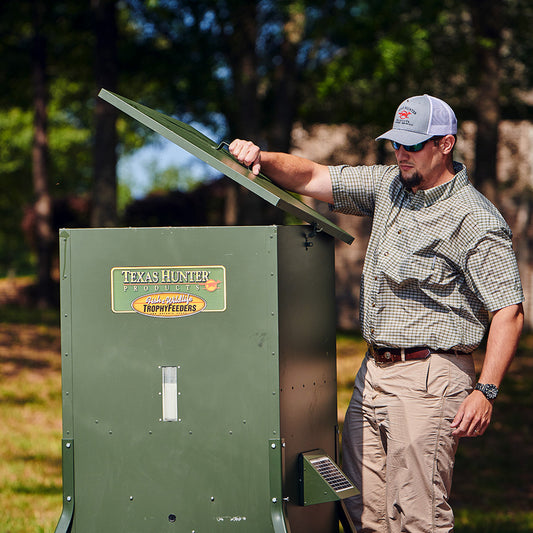 Man opening the lid of a Texas Hunter 425 lb feeder in an outdoor setting
