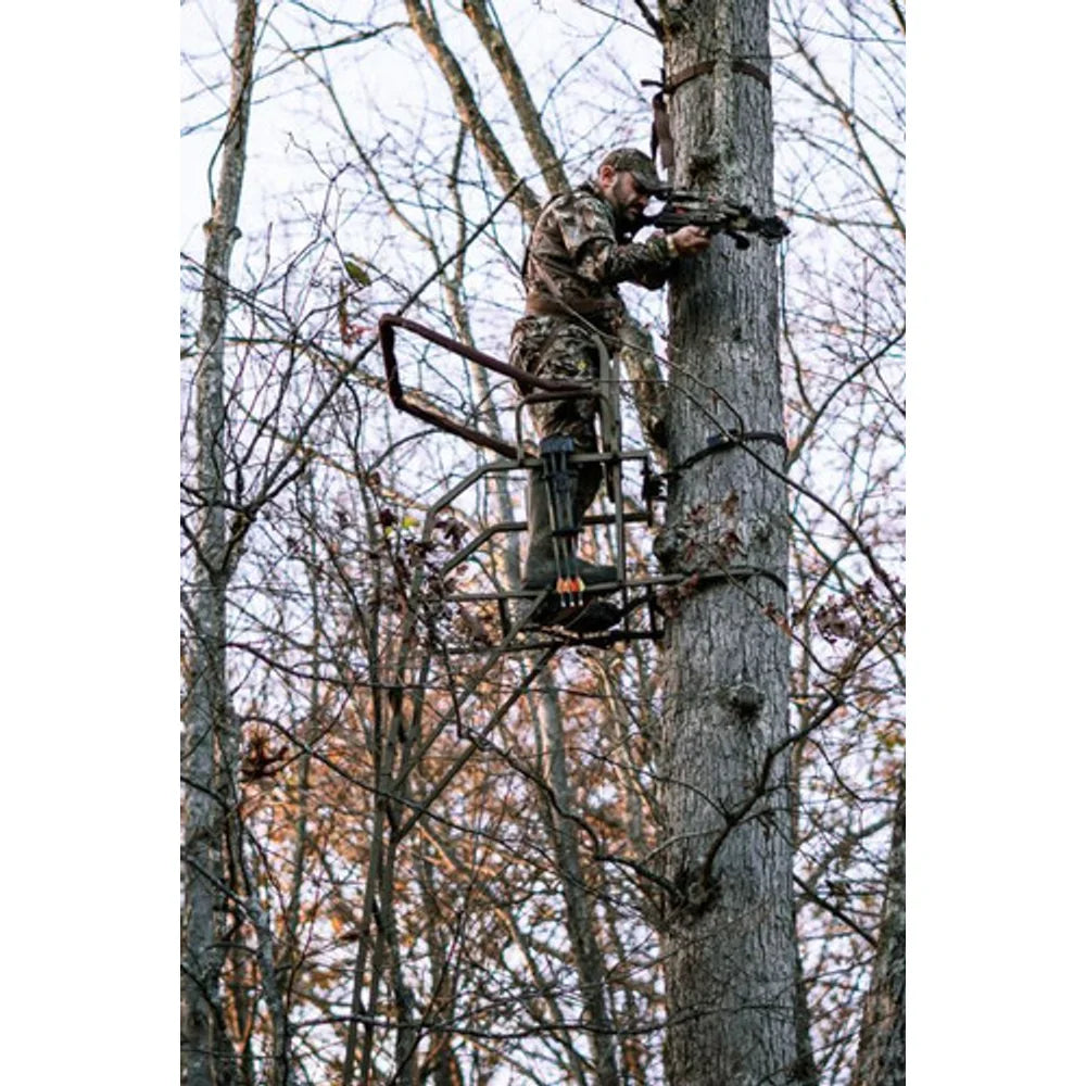 Hunter using Trophy Treestands Strike Eagle ladder stand in tree aiming a crossbow during hunt